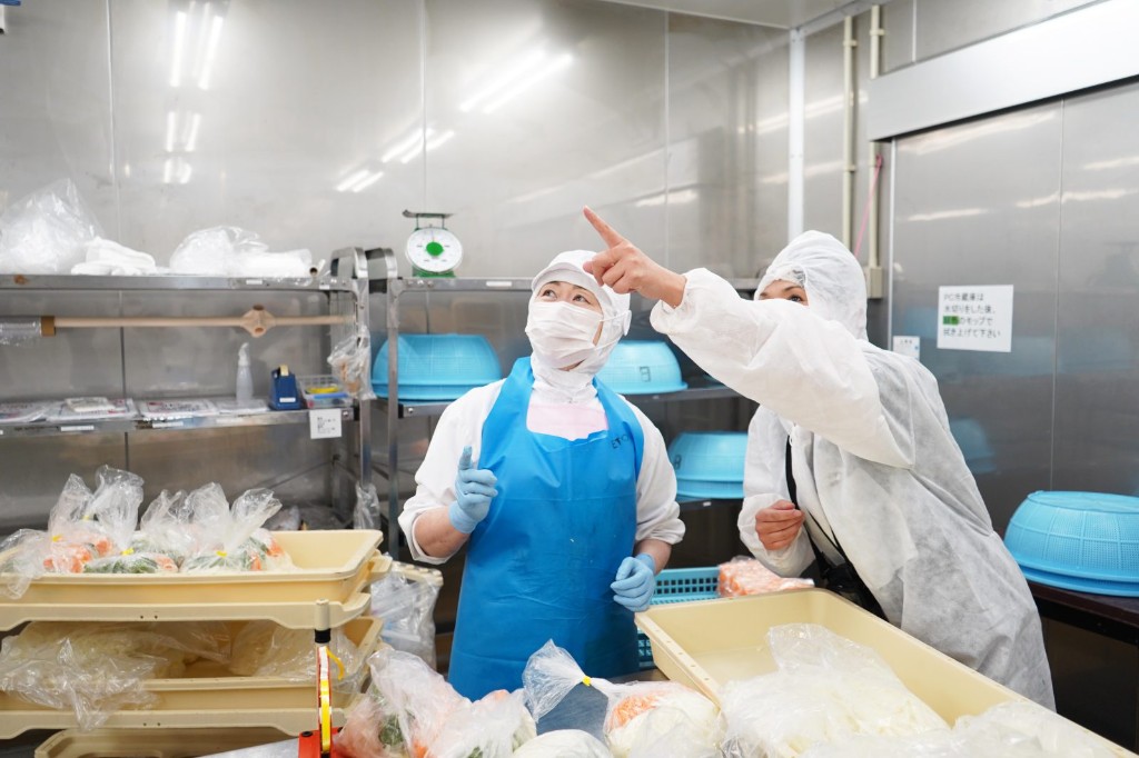 食品工場で作業の位置を指さして説明する人